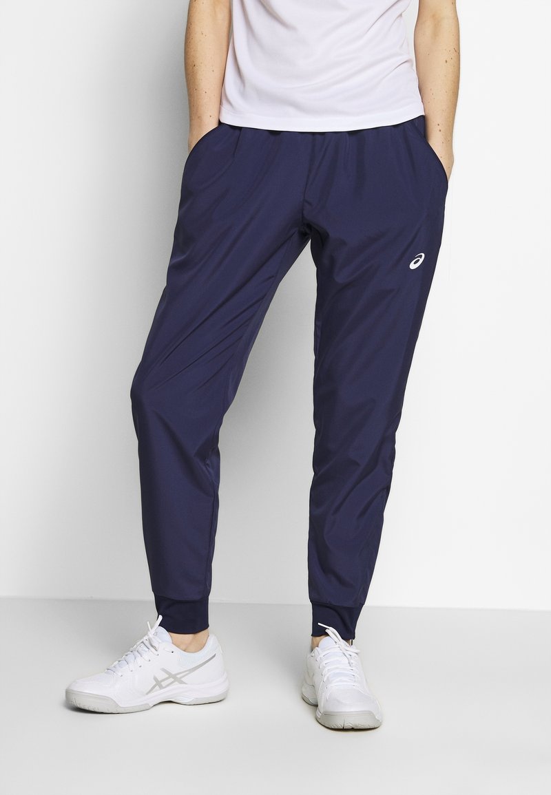 Námořnické sportovní kalhoty s úzkým střihem, elastickým pasem, bočními kapsami a malým logem na stehně, doplněné bílými teniskami.