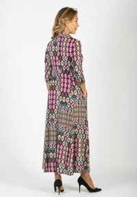 Maxi sukienka z wielokolorowym wzorem w diamenty w odcieniach różu, turkusu i brązu, z rękawami o długości trzy czwarte oraz bocznymi kieszeniami. Czarne szpilki.