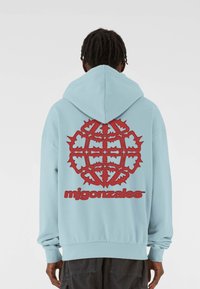 Hele sinine dressipluus suure punase graafikaga seljal, millel on keeruline disain ja tekst "mjgonzales." Pehme tekstuur, lõdva istuvusega.