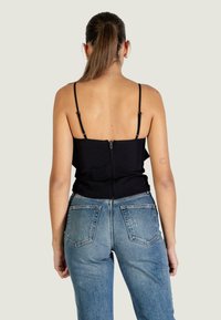 Zwart nauwsluitend topje met dunne spaghetti bandjes en een rits aan de achterkant, gecombineerd met lichtblauwe hooggetailleerde jeans met klassieke zakken.