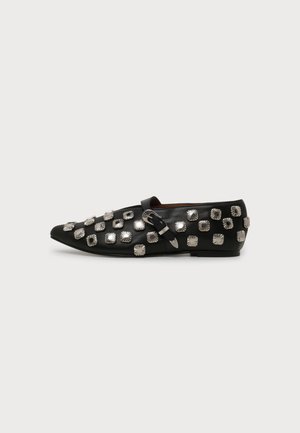 Black leather flat shoe with pointed toe, silver square studs, and a decorative buckle strap on a plain background.