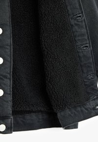Musta farkkutakki, jossa on karhea musta fleece-vuori. Takissa on hopeiset nepparit ja näkyvät ompelusaumat reunoilla.