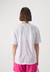 Hvit t-skjorte i bomull med korte ermer, med en nøkkelhullutskjæring bak. Glatt tekstur, avslappet passform, kombinert med rosa shorts.