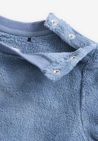 Fleece-Pullover in Hellblau, mit einer weichen Textur, Druckknöpfen und einem gerippten Kragen. Detaillierte Naht entlang der Kanten.