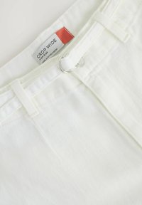 Jean blanc cropped taille haute large avec double anneaux argentés sur la boucle de ceinture et une étiquette indiquant la taille et l’origine.