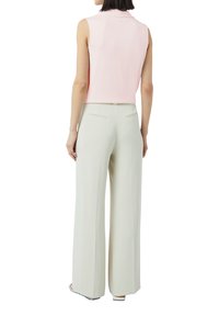 Różowa bluzka bez rękawów o lekko skróconym kroju, zestawiona z beżowymi spodniami na wysokim stanie i szerokimi nogawkami, z dwoma tylnymi kieszeniami.