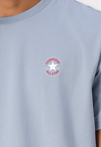 Hele sinine puuvillane T-särk, millel on ümar kaelus ning rinna peal väike punase ja valge värviga "Converse All Star" logo.