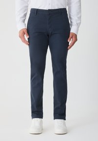 Námornícke modré chino nohavice so slim fit, vyrobené z bavlny, s bočnými vreckami, predným zapínaním na gombík a v kombinácii s bielymi teniskami.
