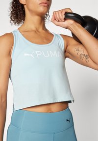 Jasnoniebieski krótki top na ramiączkach z okrągłym dekoltem i logo, w połączeniu z niebieskimi legginsami o wysokim stanie z małym czarnym logo.