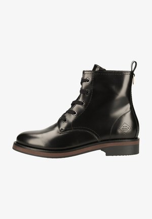 Bota de tobillo de cuero negro brillante con cordones en la parte delantera, ribete de suela marrón, lengüeta en el talón y pequeño parche con logotipo cerca del tobillo.