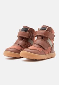 Calzature in pelle marrone con due cinturini in Velcro, suola in gomma e colletto imbottito. Presentano un design testurizzato e accenti marrone chiaro.