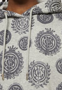 Šedá mikina s černými kruhovými emblémy obsahujícími písmena, vavřínové věnce, koruny a šňůrky s kovovými koncovkami.