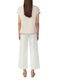 Beige T-shirt met korte mouwen en rode bies, gecombineerd met witte wijde broek, met een relaxte pasvorm en zachte textuur. Geaccentueerd met sandalen.