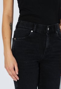 Hoch taillierte schwarze Jeans aus Denim mit einer glatten Textur, fünf Taschen, einem Reißverschluss und metallenen Knopfdetails.