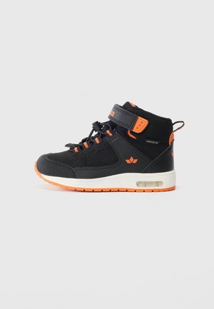 Svart og oransje høyhælte sneakers med borrelås, snørebåndsjustering, hvit midtsåle og luftputesåle på en ensfarget bakgrunn.