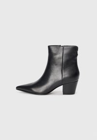 Bottine en cuir noir avec un bout pointu, un talon épais, une texture lisse et une fermeture éclair à l'arrière pour un enfilage facile.