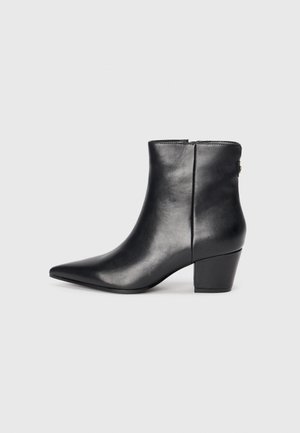 Bottine en cuir noir avec un bout pointu, un talon épais, une texture lisse et une fermeture éclair à l'arrière pour un enfilage facile.