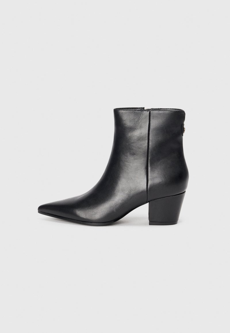Bottine en cuir noir avec un bout pointu, un talon épais, une texture lisse et une fermeture éclair à l'arrière pour un enfilage facile.