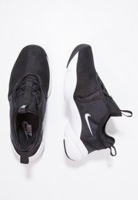 Svarta mesh-sneakers med en vit sula, med en slip-on design, dragremmar och en liten vit Nike swoosh-logotyp på sidan.