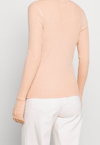 Maglia a maniche lunghe e rigata in un delicato pesca, con righe verticali. Presenta un design aderente e aperture per il pollice alle estremità delle maniche.