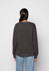 Tmavě šedá mikina s volným střihem, kulatým výstřihem a spadlými rameny. Kombinována s světle modrými, volně střiženými džínami.