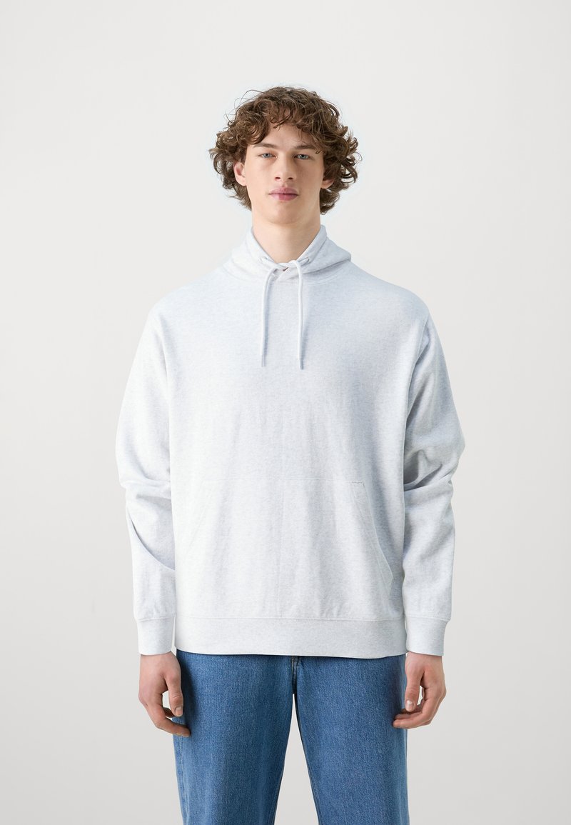 Lichtgrijze hoodie met een hoge hals, koordjes, een kangoeroezak en lange mouwen; gecombineerd met blauwe jeans voor een casual look.
