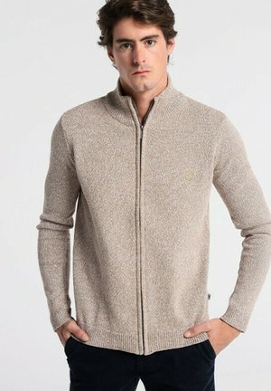 Beige knitted zip-up sweater with a high collar, long sleeves, and ribbed cuffs. Features a small logo on the left chest.