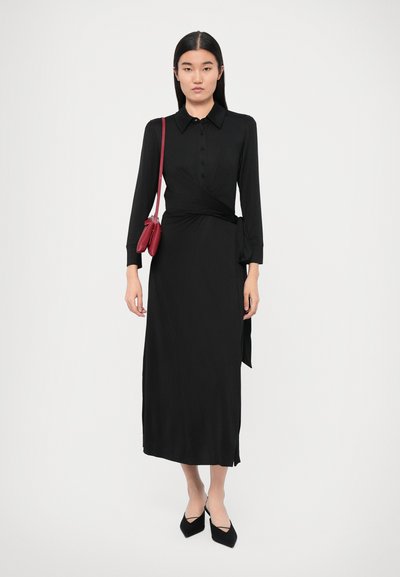 Rochie neagră cu mâneci lungi, cu nasturi în față și cordon în talie. Asortată cu pantofi negri cu vârf ascuțit și o geantă roșie de tip crossbody.