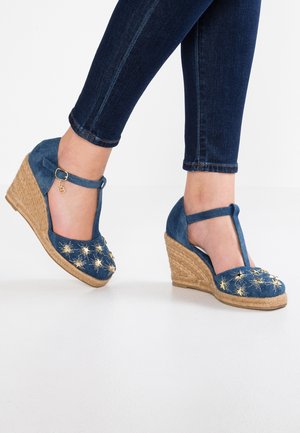 Denim skud med kilehæl og T-strop-design, prydet med guldstjernebroderi og en juteindpakket hæl. Blå farve og tekstureret overflade.