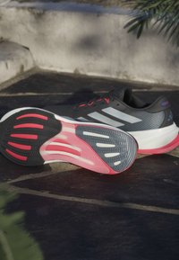 Zapatillas deportivas para hombre con parte superior en gris, acentos rojos y una suela rayada con detalles en negro y rosa para una mayor tracción.
