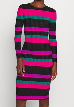 Robe ajustée à manches longues en maille côtelée avec des rayures horizontales noires, magenta, violettes et bleu sarcelle, portée par une personne debout devant un fond uni.