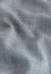 Tissu gris clair avec un motif pied-de-poule fin et de subtiles lignes à carreaux bleues, présenté avec des plis doux et des détails de texture.