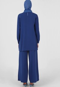 Blå tunika og brede bukser sæt, der har en høj hals, lange ærmer og blødt stof med minimale detaljer.
