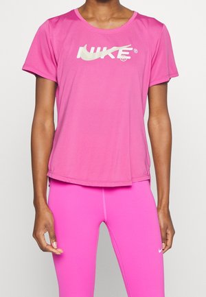 Femme portant un t-shirt Nike rose vif à manches courtes et un legging rose assorti, debout devant un fond clair uni.