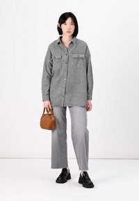 Black and white checkered oversized shirt, gray jeans, black platform shoes, and a small brown handbag, against a plain white background.