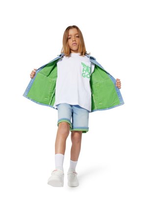 Chaqueta de denim de exterior azul claro y interior verde, camiseta blanca con gráficos verdes, pantalones cortos azul claro con detalles verdes, zapatillas blancas.