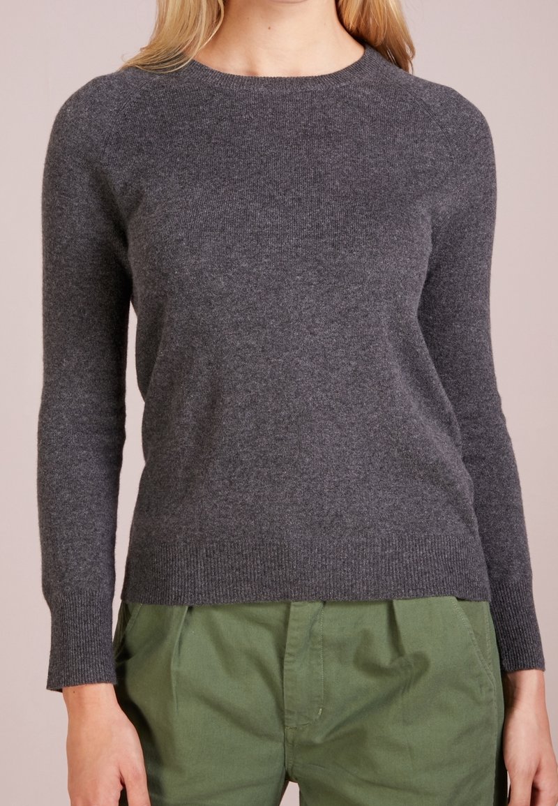 Grå stickad tröja med rund halsringning och långa ärmar. Mjuk textur och ribbat kantdetalj. Matchas med gröna tygbyxor.
