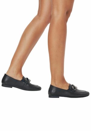 Mocasines de cuero negro con suela plana, que presentan una correa decorativa con un acento metálico circular y un acabado de textura suave.