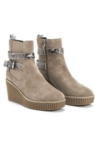 Stivali ankle in suede beige con suola a zeppa, caratterizzati da una fascia testurizzata argentata e chiusura lampo laterale. Suola rigata per una migliore aderenza.