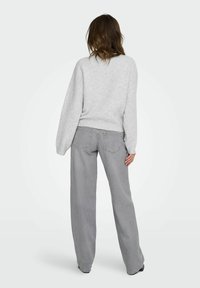 Svetle šedý oversized svetr s klesajícími rameny a žebrovaným lemem, doplněný o svetle šedé široké kalhoty s kapsami na zadní straně.