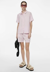 Camicia a maniche corte a righe rosa chiaro e bianco e pantaloni corti abbinati, abbinati a sandali beige pelosi e una borsa a tracolla nera.