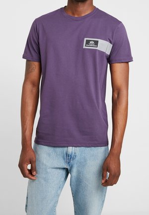 Violetti puuvillapaita lyhyillä hihoilla, pyöreällä kaula-aukolla ja harmaalla korostesiimalla. Rinnassa on suorakulmainen logopainatus.