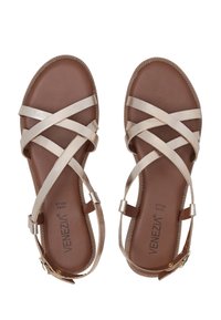 Braune Sandalen mit metallisch goldenen, kreuzenden Riemen, einer glatten Lederinnensohle und einem Knöchelriemen mit einer goldenen Schnallenverzierung.