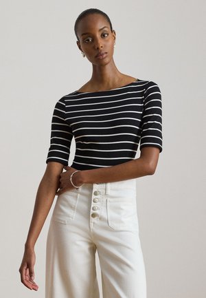 Femme portant un haut à rayures horizontales noires et blanches avec des manches jusqu'au coude et un pantalon blanc taille haute avec des boutons.