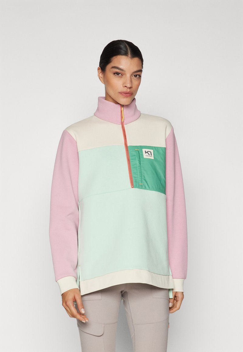 Farverig pullover sweatshirt lavet af blødt stof. Har en høj krave, halvdels lynlås og en brystlomme i grøn med et logo. Farverne inkluderer pink, mintgrøn og creme.