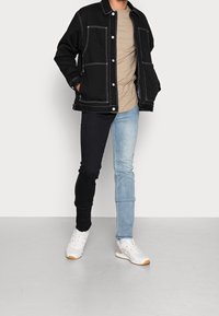 Black jacket with white stitching, beige t-shirt, black and light blue split jeans, and white sneakers with brown accents.