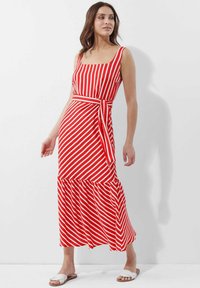 Maxikleid mit rot-weißen vertikalen Streifen, quadratischem Ausschnitt, tailliertem Bund, ausgestelltem Rock und gestuftem Saum. Das Model trägt flache Sandalen.