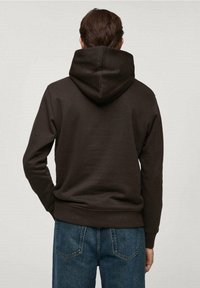 Felpa marrone in morbido tessuto con cappuccio spazioso, polsini e orlo a coste, indossata con jeans blu. Design pulito e minimalista.