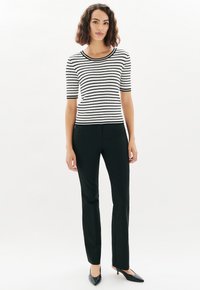 Top de manga corta a rayas blancas y negras, ajustado, combinado con pantalones negros de corte sastre y estilizadas tacones negros de punta. Textura suave, ajuste casual.