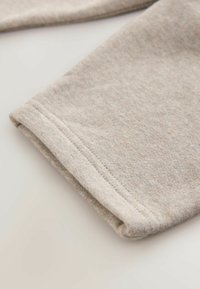 Beež, pehme tekstuuriga kangas voltidega äärega ja nähtava õmblusdetailiga. Lihtne, kaunistusteta disain, mis sobib igapäevaseks kandmiseks.